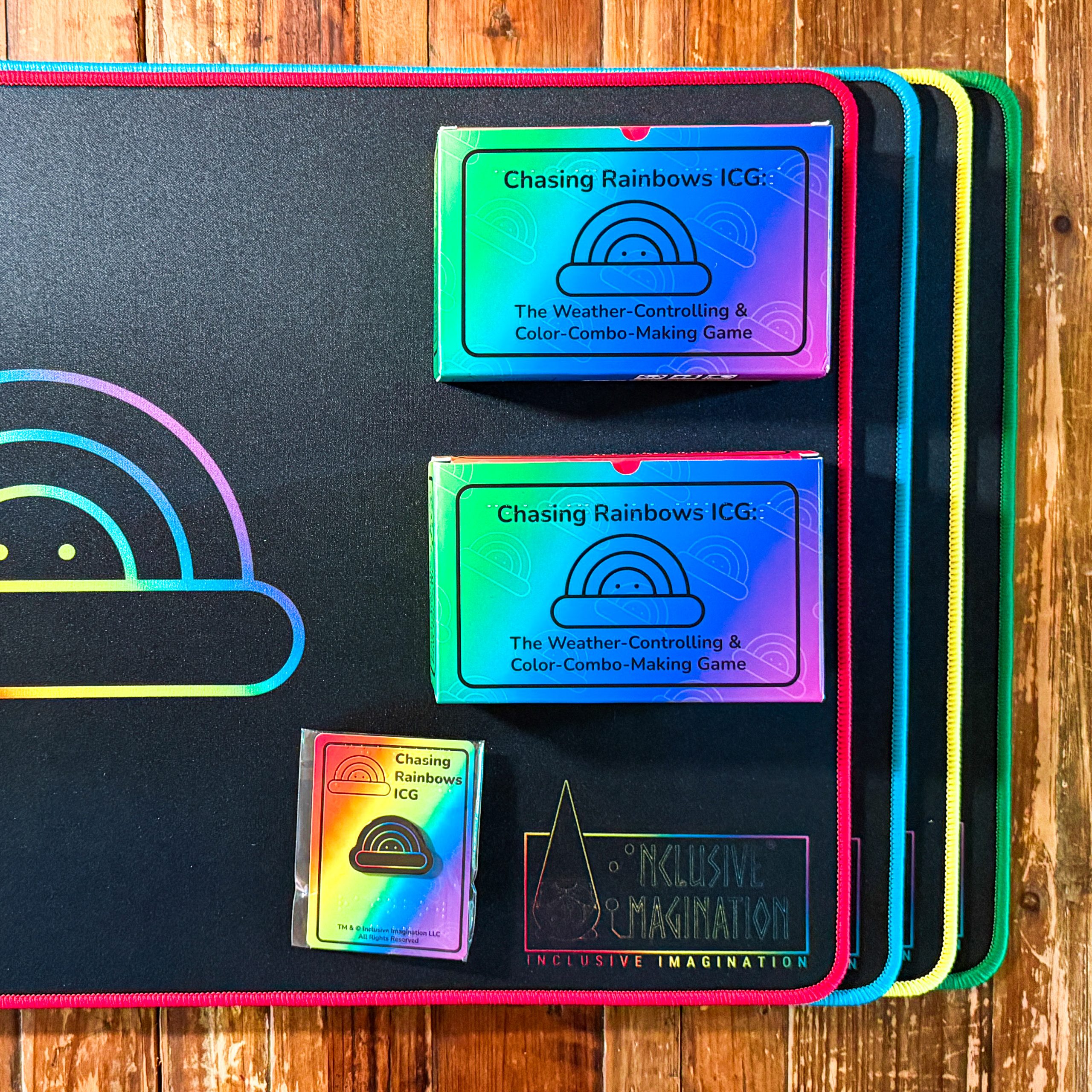 2 Chasing Rainbows Games, 1 Rainbow Logo Pin, 1 Red Playmat, 1 Blue Playmat, 1 Yellow Playmat, and 1 Green Playmat on a Table